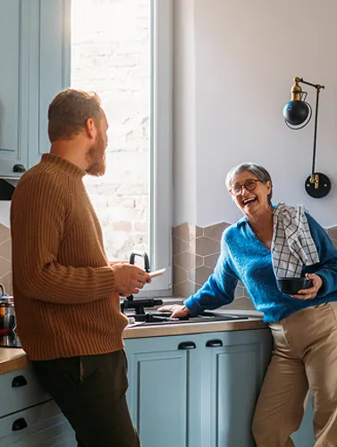 A man and woman are positioned in a cozy kitchen, smiling as they collaborate on meal preparation.
