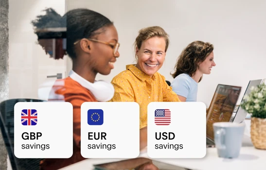 People working at an office desk, smiling and laughing, with foreign currency cards overlayed on top of the image