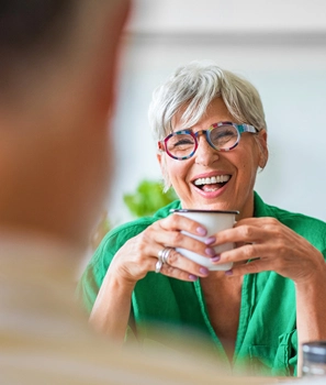 A woman wearing glasses and a green shirt smiles warmly at the camera.