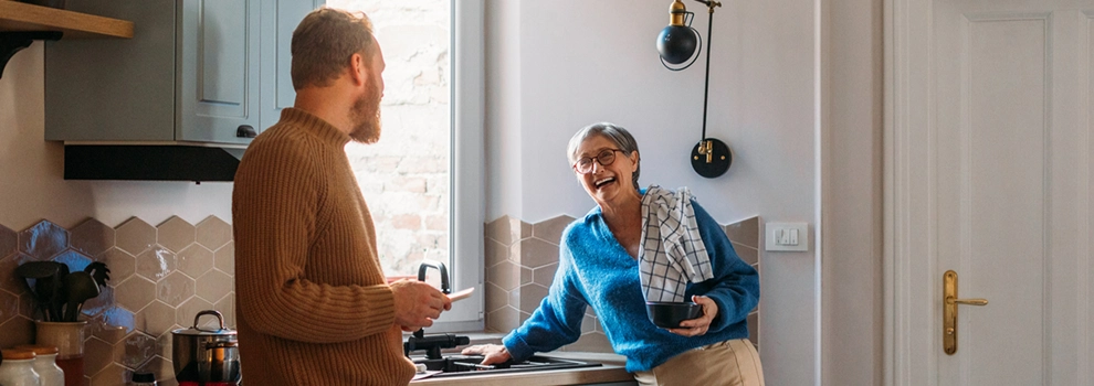 A man and woman are positioned in a cozy kitchen, smiling as they collaborate on meal preparation.