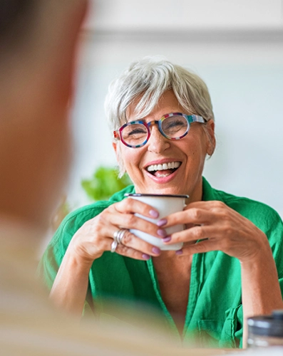 A woman wearing glasses and a green shirt smiles warmly at the camera.